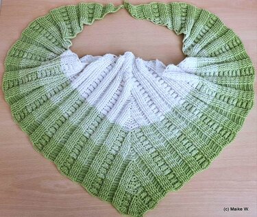 Gehäkeltes Dreieckstuch in Weiß und Hellgrün mit Rippen- und Lochmustern, flach auf einer Holzoberfläche ausgelegt.