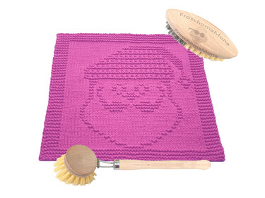 Gestricktes pinkes Spültuch mit Weihnachtsmann-Design und zwei Holzspülbürsten auf weißem Untergrund.