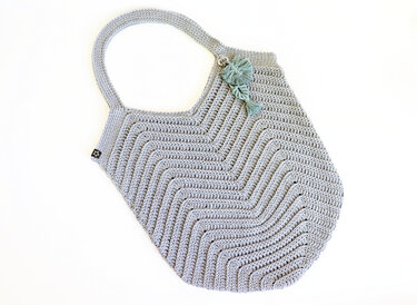 Light grey crocheted shoulder bag with chevron stitch, single handle and tassel charm.