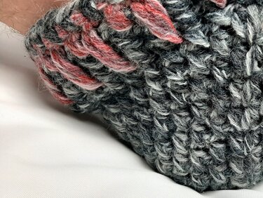 Nahaufnahme eines gehäkelten grauen Hausschuhs mit rosafarbenem Streifen