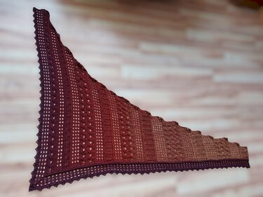 Triangular crocheted shawl laid flat, burgundy to brown gradient with lace panels and scalloped edge