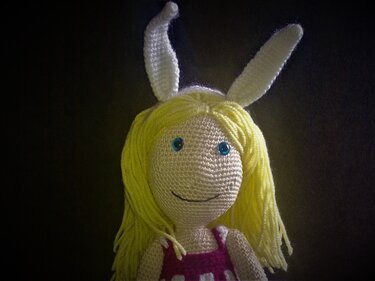 Handgehäkelte Amigurumi-Puppe mit langen blonden Haaren, blauen Augen, rosa-weiß gestreiftem Kleid und weißen Hasenohren.