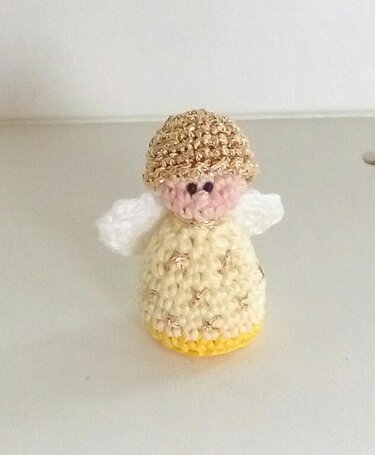 Kleines gehäkeltes Engel-Amigurumi mit goldener Mütze, cremefarbenem Kleid und weißen Flügeln