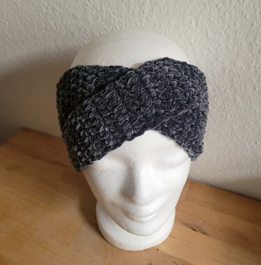 Dunkelgraues, gehäkeltes Stirnband aus flauschigem, samtartigem Garn mit gedrehter Vorderpartie auf einer Schaufenster- bzw. Styroporkopf-Büste.