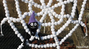 Schwarze gehäkelte Spinne mit lila Hexenhut auf weißem gehäkeltem Spinnennetz