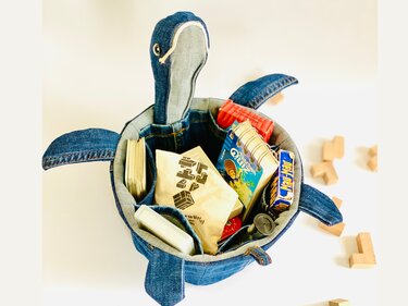 Jeans-Utensilo in Schildkrötenform mit Innentaschen, gefüllt mit Spielzeug und Karten
