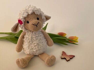Detailansicht gehäkeltes Amigurumi-Lämmchen mit flauschigem Körper und rosa Blüte am Ohr