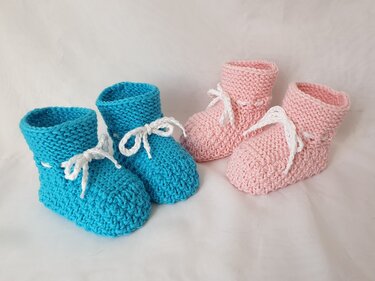 Zwei Paar gestrickte Babyschuhe, ein türkisfarbenes und ein rosafarbenes Paar, mit weißen Schnürbändern