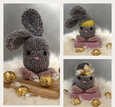Graues, gehäkeltes Amigurumi-Häschen mit rosa Pfötchen und Nase auf flauschigem Untergrund, geeignet als Osterversteck.