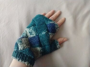 Hand mit gestricktem, fingerlosem Handschuh in Blau-, Grün- und Weißtönen auf hellem Untergrund