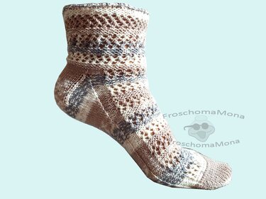 Gestrickte Socke in Braun, Beige und Grau mit Ajourmuster vor hellblauem Hintergrund
