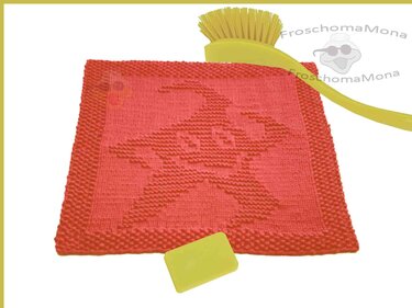 Rotes, quadratisches Stricktuch mit eingearbeitetem Froschmotiv, daneben eine gelbe Bürste und ein kleines gelbes Rechteck.
