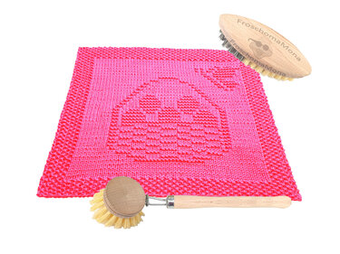 Quadratisches pinkes Stricktuch mit eingestricktem Hasenmotiv, daneben zwei Holzbürsten.