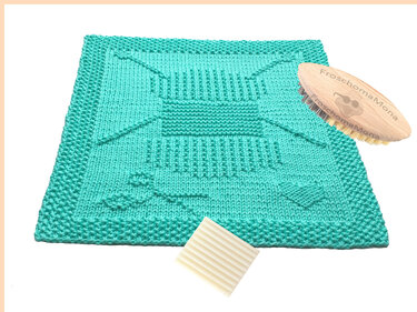 Mintgrünes gestricktes Spültuch mit Reliefmustern, neben Holzbürste und Reinigungspad
