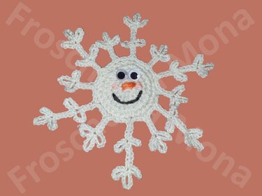 Kompakte weiß gehäkelte Schneeflocke mit aufgenähtem Gesicht, Wackelaugen und Karottennase