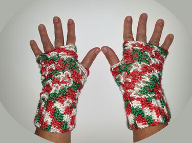 Zwei Hände mit gehäkelten, fingerlosen Stulpen in Rot, Weiß und Grün mit sichtbarer Daumenöffnung
