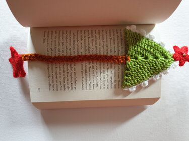 Gehäkeltes grünes Tannenbaum-Lesezeichen mit weißem Zackenrand, roten Sternen und schmalem braunem Band in aufgeschlagenem Buch