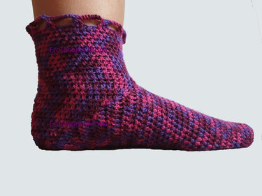 Gehäkelte Socke in Lila‑Pink‑Melange mit dekorativem Wellenbündchen, am Fuß getragen.