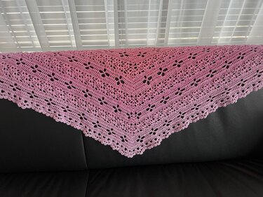 Rosa gehäkeltes Dreieckstuch mit Loch- und Blütenmuster über schwarzem Sofa drapiert