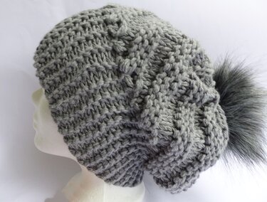 Graue Strickmütze mit strukturiertem Muster und großem grauen Bommel