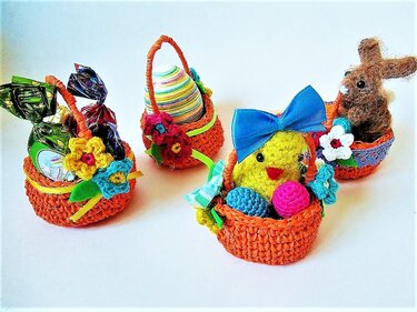 Vier kleine gehäkelte orangefarbene Osterkörbchen mit Blumen, gefüllt mit Küken, Hase, Eiern und Süßigkeiten