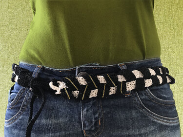 Handgehäkelter Boho-Gürtel in Schwarz-Weiß mit goldfarbenen Ketten und seitlicher Schnürung an einer Jeans