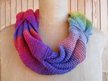 Knitted cowl scarf with rainbow gradient colors on a dress form.