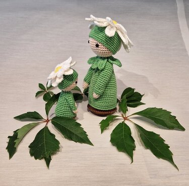 Zwei gehäkelte Amigurumi-Puppen in grünen Kleidern mit weißen Margeritenhüten
