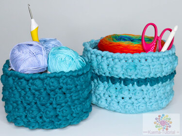 Zwei gehäkelte Körbe in Blau- und Türkistönen, gefüllt mit Garn, Häkelnadel und Schere.