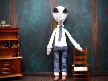 Gehäkelter Alien-Amigurumi in Hemd und Krawatte neben Miniaturmöbeln