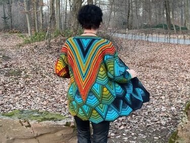 Rückansicht einer Person in mehrfarbiger Strickjacke mit großem V‑förmigem Zackenmuster