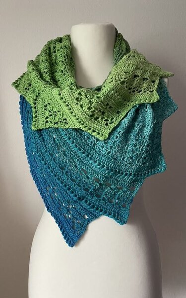 Gehäkelter dreieckiger Drachenschwanz-Schal in Grün- und Blautönen auf weißer Schaufensterpuppe