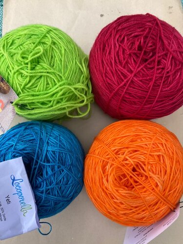 Vier Garnknäuel in Limettengrün, Pink, Türkis und Orange auf hellem Untergrund.