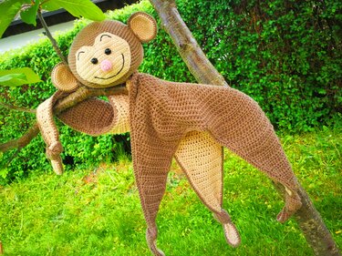 Gehäkeltes braun-beiges Schmusetuch in Affenform an einem Baumzweig hängend