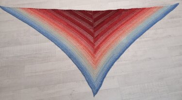 Gehäkeltes dreieckiges Tuch mit Farbverlauf von Rot zu Blau flach auf hellem Boden ausgelegt