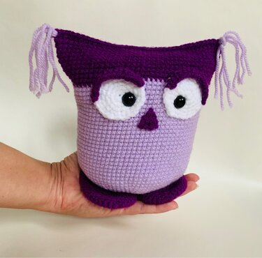 Gehäkelte Amigurumi‑Eule in Flieder und Dunkellila auf einer Hand gehalten