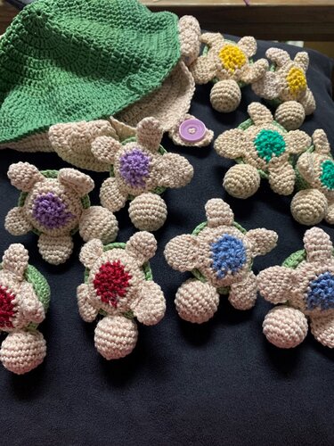 Mehrere kleine gehäkelte Schildkröten-Amigurumi in Beige mit bunten Mittelpunkten, grünes gehäkeltes Teil und Knopf auf dunklem Untergrund