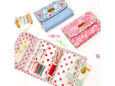 Offenes Näh-Utensilo aus gemustertem Stoff mit Schere, Garn, Nadeln und Maßband; zwei gesteppte Stofftäschchen daneben.