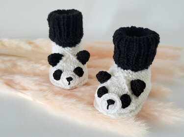 Paar gestrickte Panda-Babyschuhe auf hellem, weichem Hintergrund