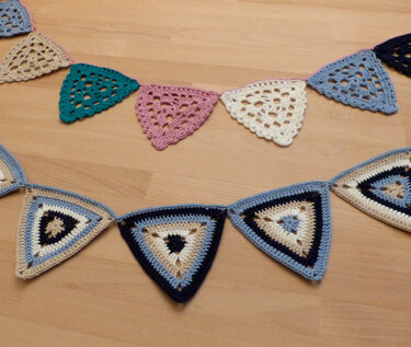 Nahaufnahme gehäkelter dreieckiger Wimpel in Pastell- und Blautönen auf Holzboden