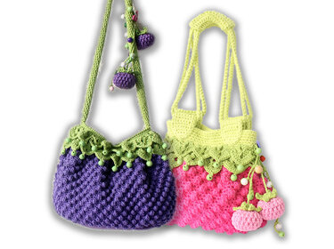 Two crocheted shoulder bags: purple with green scalloped trim and purple berry charms; pink with green scalloped trim, yellow straps, and pink berry charms.