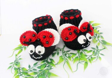 Handgehäkelte Babyschuhe im Marienkäfer-Design, schwarz mit roten Flügeln, weißen Gesichtern und schwarzen Perlenaugen.