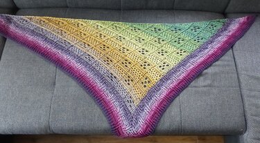 Gehäkeltes Dreieckstuch in Magenta, Gelb und Grün mit Lochmuster auf grauem Sofa