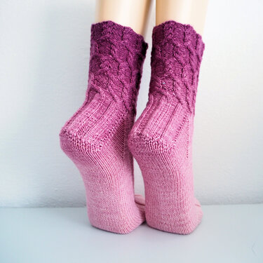 Close-up of pink to purple ombre knitted socks with cable cuff and ribbed ankle.
