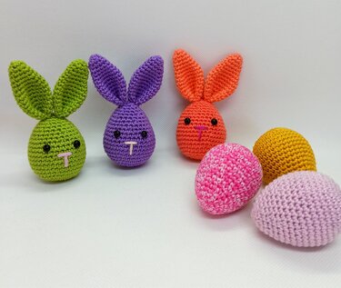 Three colorful amigurumi bunnies and three crocheted eggs arranged on a white surface