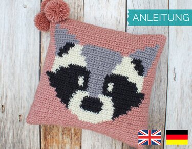 Rosa gehäkelter Kissenbezug mit stilisiertem Waschbärgesicht und Bommel