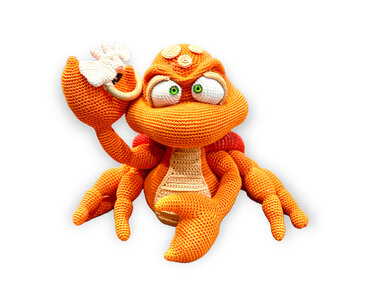 Orange gehäkelte Amigurumi-Krabbe mit grünen Augen und kleinem weißen Anhänger