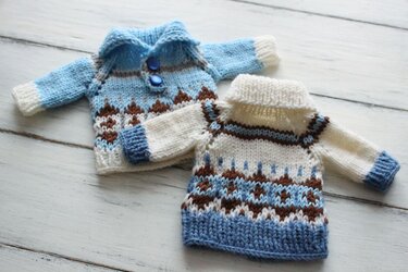 Two miniature knitted sweaters: blue collared with buttons and cream roll-neck with patterned motifs.