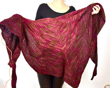 Person hält gestricktes Dreieckstuch in Pink- und Brauntönen mit Rippen- und Chevron-Muster vor weißem Hintergrund.