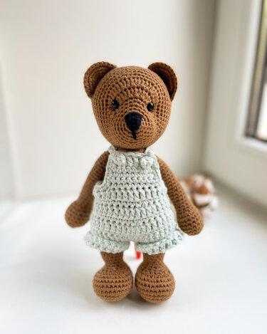 Kompakter brauner Amigurumi-Teddy trägt hellen Häkelstrampler